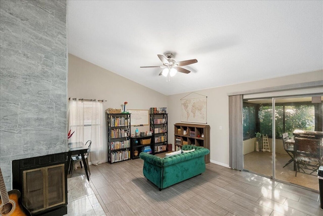 living area featuring ceiling fan, a fireplace, and vaulted ceiling