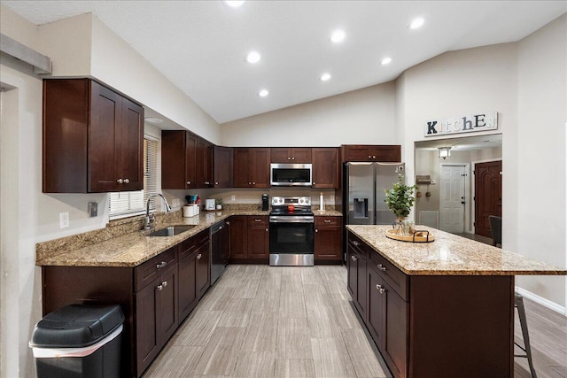 kitchen featuring dark brown cabinetry, sink, a kitchen breakfast bar, stainless steel appliances, and light stone countertops