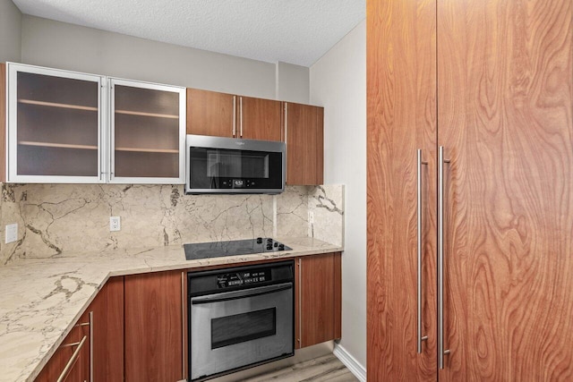 kitchen featuring appliances with stainless steel finishes, light stone countertops, a textured ceiling, decorative backsplash, and light wood-type flooring