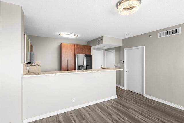 kitchen with stainless steel refrigerator with ice dispenser, kitchen peninsula, dark wood-type flooring, and a textured ceiling