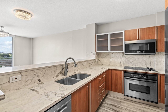 kitchen with decorative backsplash, glass insert cabinets, appliances with stainless steel finishes, brown cabinets, and a sink