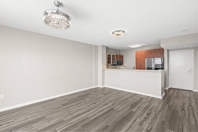 kitchen featuring baseboards, brown cabinets, wood finished floors, a peninsula, and stainless steel appliances