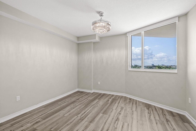 empty room featuring an inviting chandelier, light hardwood / wood-style floors, and a textured ceiling