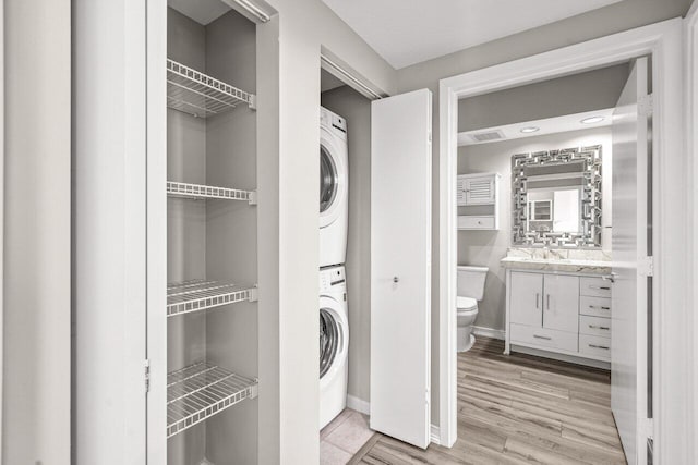 clothes washing area with stacked washer and dryer, laundry area, baseboards, light wood-style flooring, and a sink