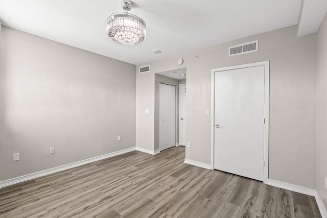 unfurnished bedroom with a chandelier, light wood-style flooring, visible vents, and baseboards