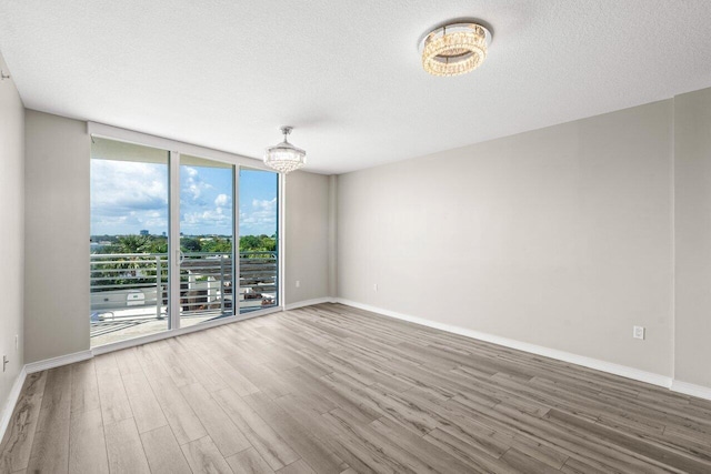 empty room featuring floor to ceiling windows, a textured ceiling, baseboards, and wood finished floors