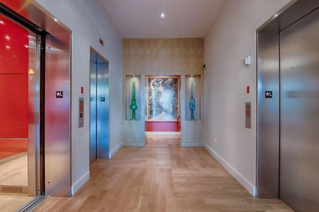 hall with light wood-style floors, elevator, and baseboards