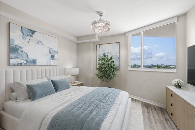 bedroom featuring a textured ceiling, light wood-type flooring, a chandelier, and baseboards