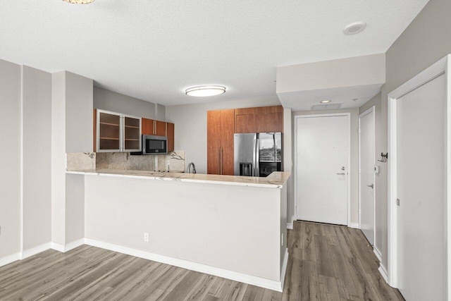 kitchen with tasteful backsplash, light wood-type flooring, kitchen peninsula, stainless steel appliances, and a textured ceiling