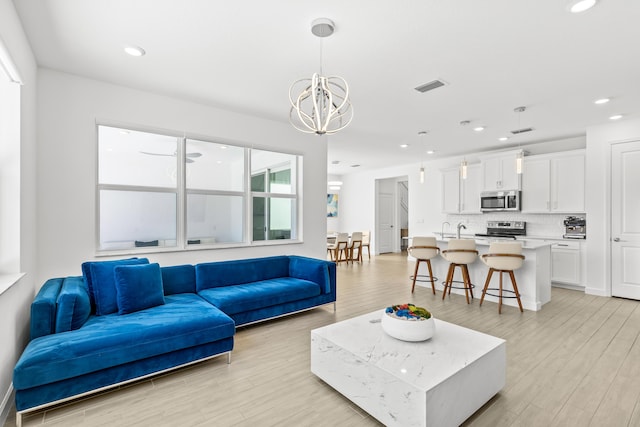 living room featuring a chandelier, sink, and light hardwood / wood-style flooring