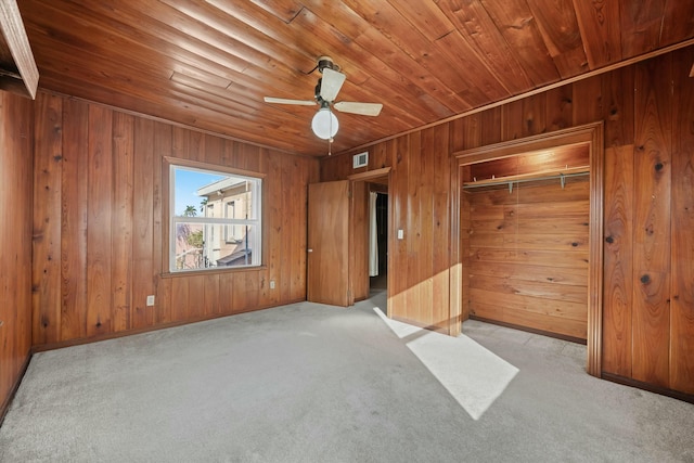 unfurnished bedroom featuring light carpet, wooden ceiling, wooden walls, and a closet