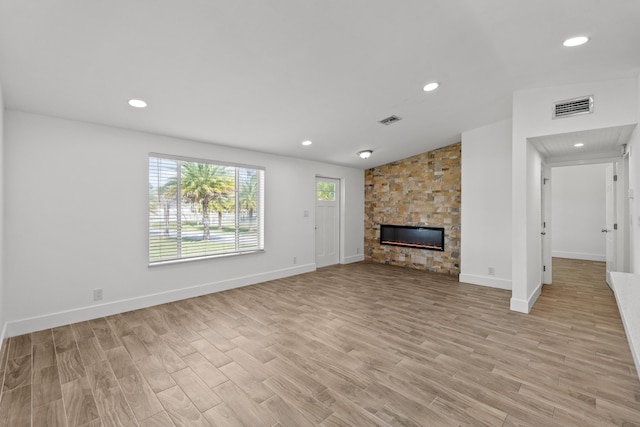 unfurnished living room with a stone fireplace and light wood-type flooring