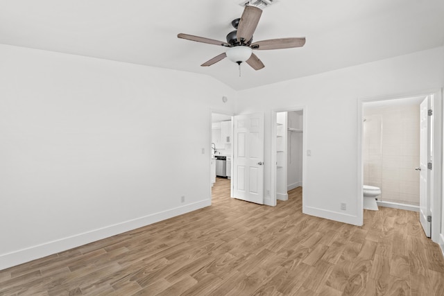 unfurnished bedroom with connected bathroom, a spacious closet, vaulted ceiling, light hardwood / wood-style flooring, and a closet