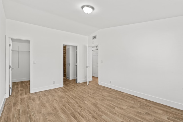 unfurnished bedroom with a closet, lofted ceiling, a spacious closet, and light hardwood / wood-style flooring