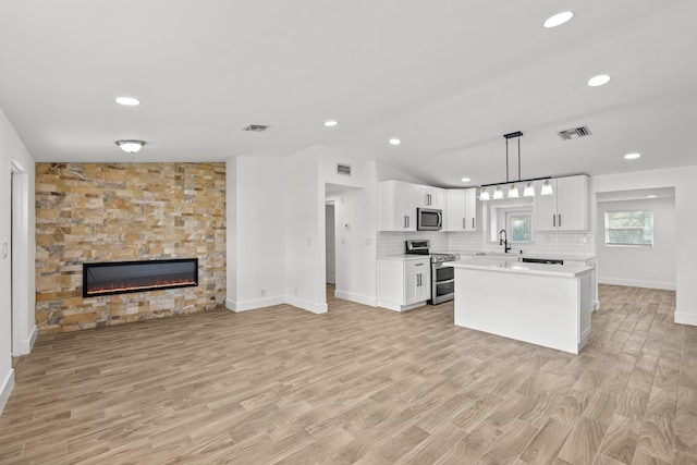 kitchen with a kitchen island, pendant lighting, a fireplace, white cabinetry, and stainless steel appliances