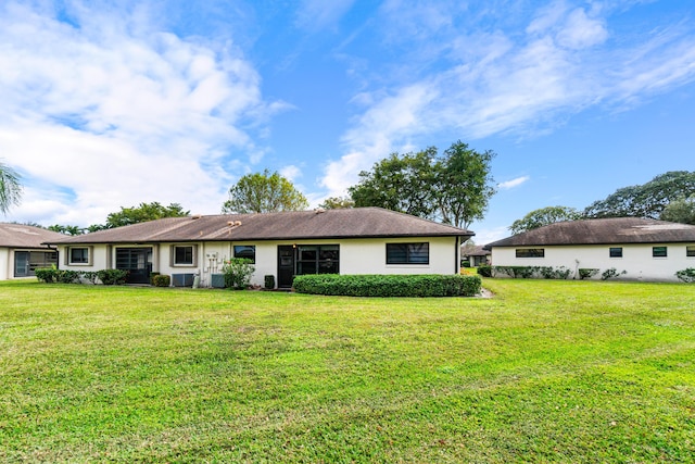 rear view of house with central AC unit and a lawn