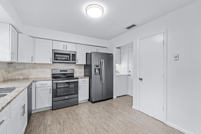 kitchen with washer / dryer, white cabinets, decorative backsplash, stainless steel appliances, and light stone countertops