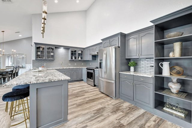 kitchen with gray cabinets, light hardwood / wood-style flooring, stainless steel appliances, light stone counters, and a center island with sink