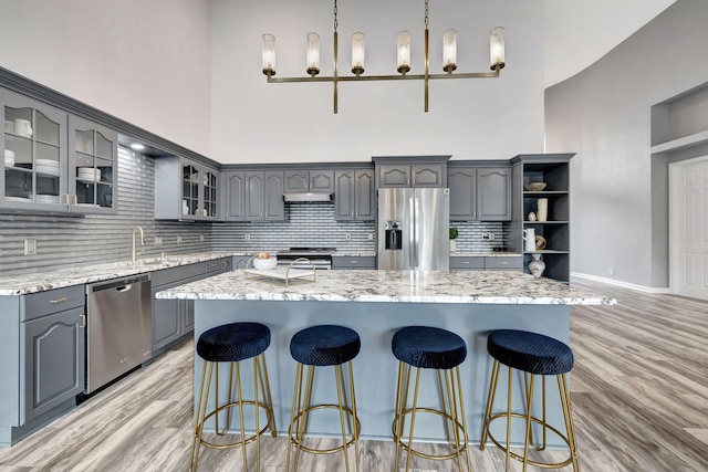 kitchen featuring gray cabinetry, hanging light fixtures, stainless steel appliances, a kitchen island, and light wood-type flooring