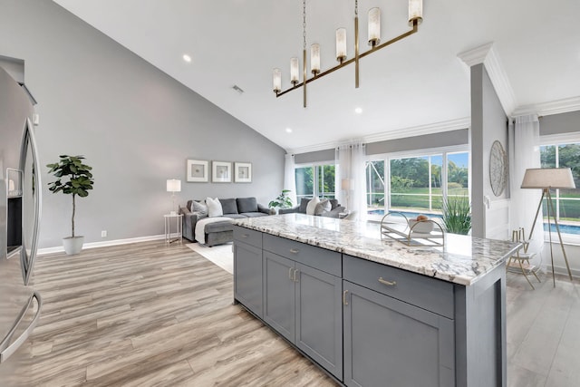 kitchen featuring gray cabinetry, hanging light fixtures, a center island, light stone counters, and crown molding