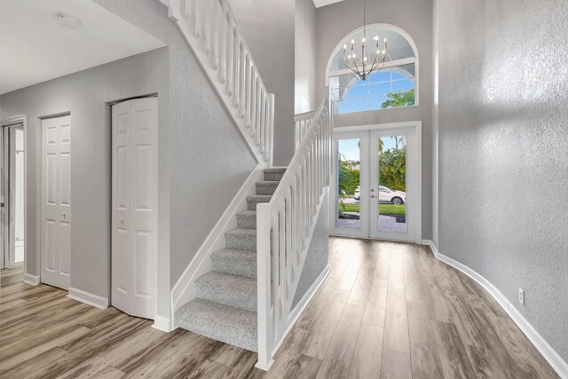 entrance foyer featuring french doors, a towering ceiling, an inviting chandelier, and light hardwood / wood-style floors