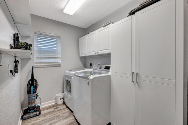 clothes washing area with cabinets, a textured ceiling, washer and dryer, and light hardwood / wood-style flooring