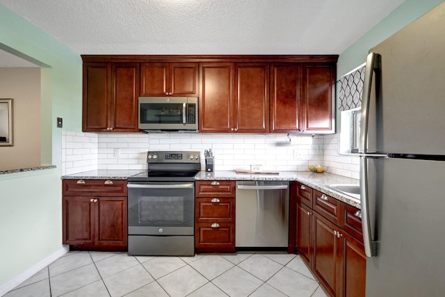 kitchen with tasteful backsplash, appliances with stainless steel finishes, light stone countertops, and light tile patterned floors