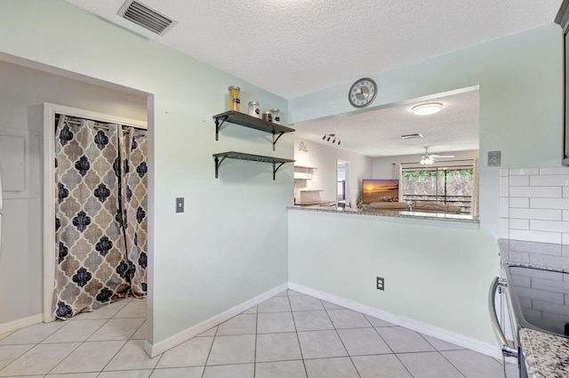 kitchen with stainless steel electric range, a textured ceiling, light tile patterned floors, kitchen peninsula, and light stone countertops