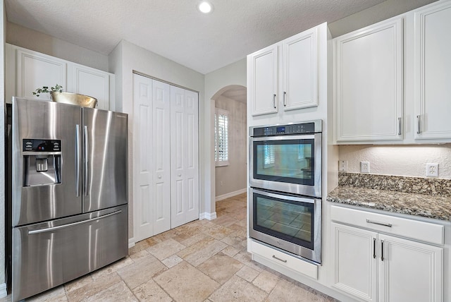 kitchen with white cabinets, dark stone countertops, stainless steel appliances, and a textured ceiling