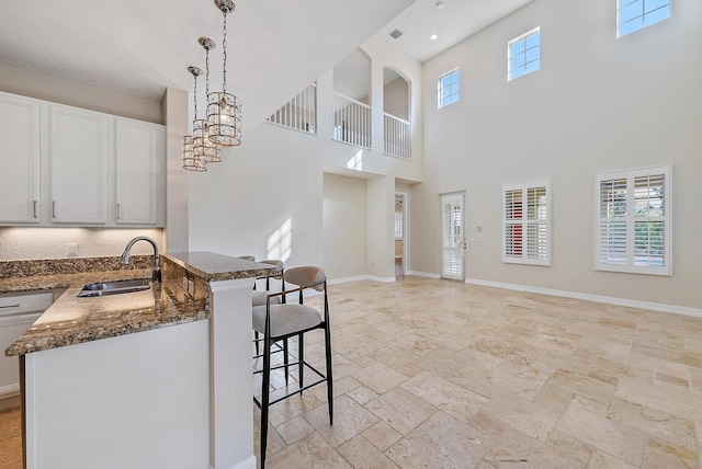 kitchen with dark stone counters, decorative light fixtures, sink, white cabinetry, and a kitchen bar