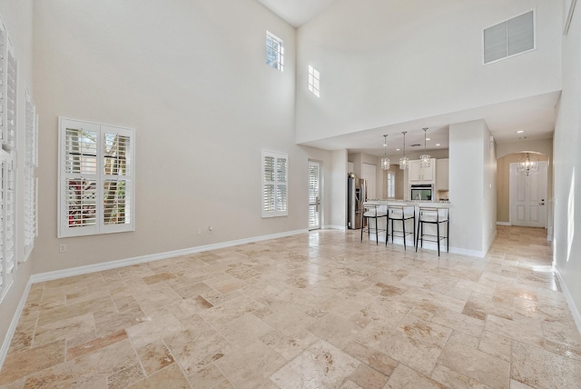 unfurnished living room featuring a notable chandelier and a towering ceiling