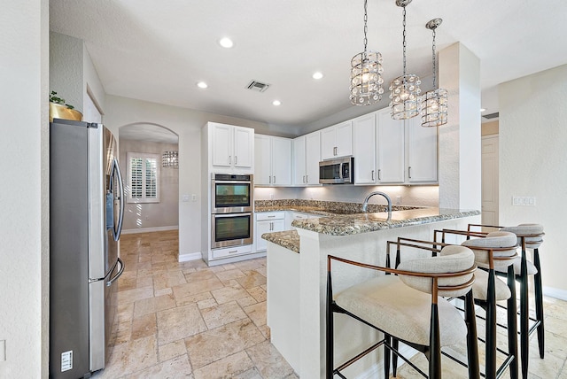 kitchen with white cabinets, dark stone countertops, appliances with stainless steel finishes, and kitchen peninsula