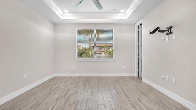 empty room with a raised ceiling, crown molding, ceiling fan, and light hardwood / wood-style floors