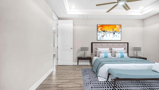 bedroom with crown molding, light hardwood / wood-style flooring, ceiling fan, and a tray ceiling