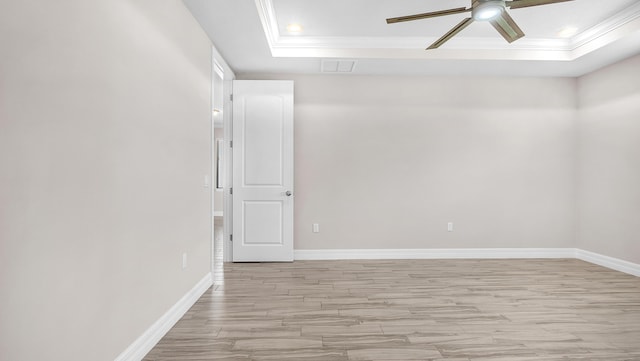 empty room with ceiling fan, ornamental molding, a raised ceiling, and light hardwood / wood-style flooring