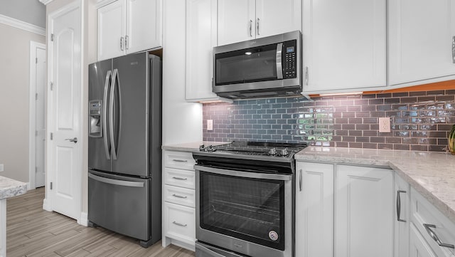 kitchen featuring stainless steel appliances, white cabinetry, light stone countertops, and backsplash