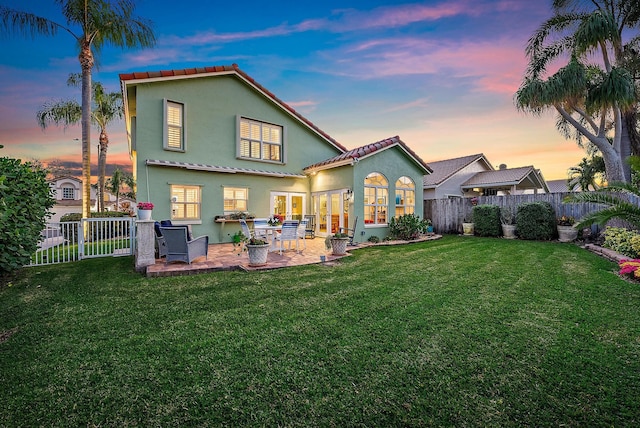 back house at dusk with a lawn and a patio area