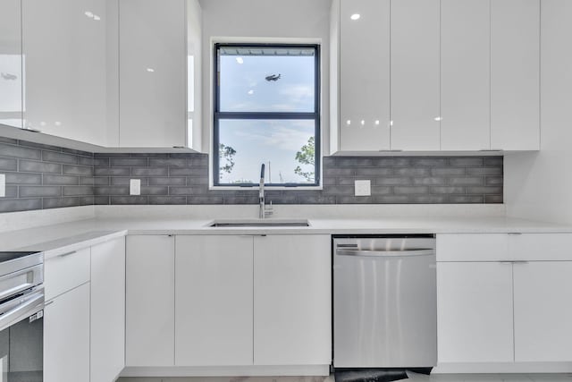 kitchen with light countertops, stainless steel dishwasher, white cabinetry, a sink, and modern cabinets