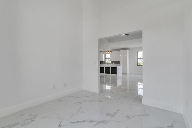 empty room with a notable chandelier, marble finish floor, and baseboards