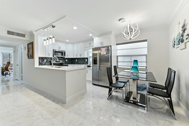 kitchen with appliances with stainless steel finishes, white cabinetry, hanging light fixtures, ornamental molding, and a notable chandelier