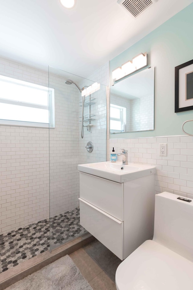 bathroom with vanity, tile patterned flooring, tile walls, and a tile shower