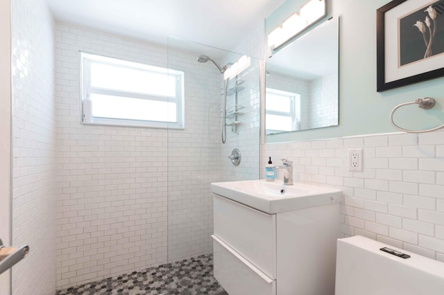 bathroom featuring tiled shower, vanity, and tile walls