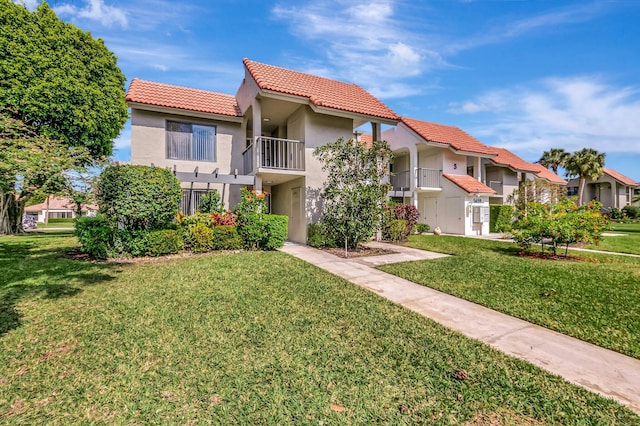 view of front of property featuring a front lawn, a tile roof, a balcony, and stucco siding