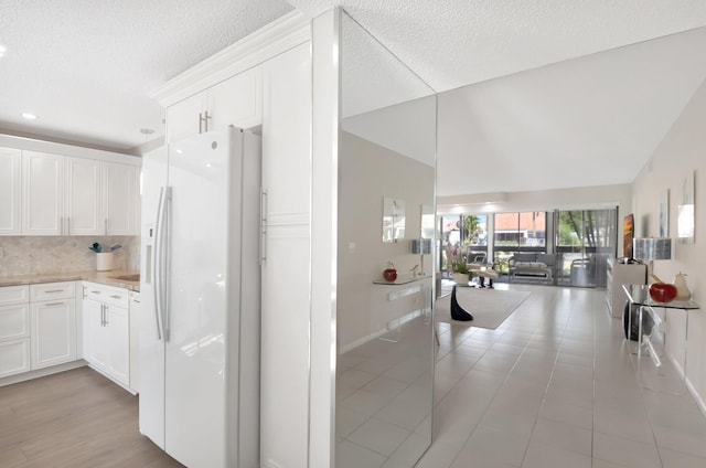 kitchen with lofted ceiling, white refrigerator with ice dispenser, white cabinets, open floor plan, and backsplash