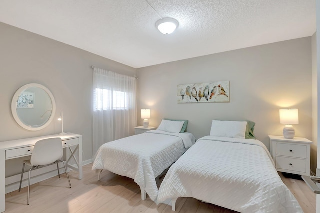 bedroom with a textured ceiling, light wood-style flooring, and baseboards