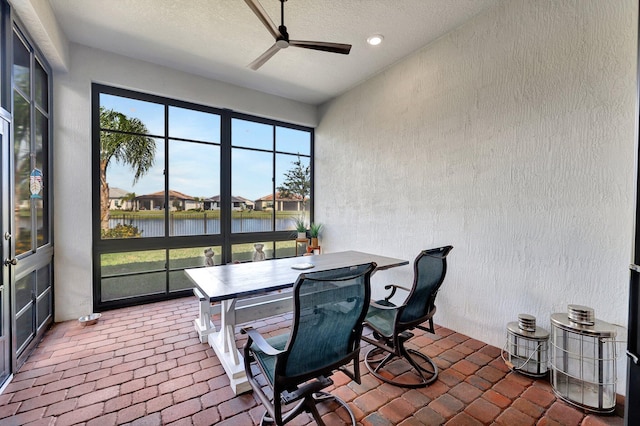 sunroom with ceiling fan and a water view