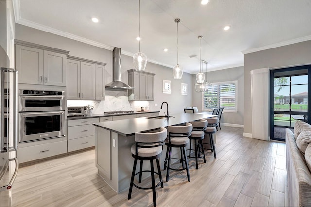 kitchen featuring appliances with stainless steel finishes, pendant lighting, sink, gray cabinetry, and wall chimney exhaust hood