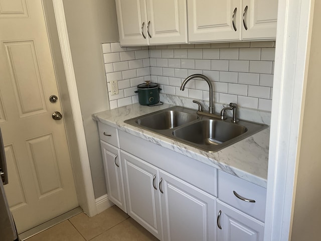 kitchen with tasteful backsplash, sink, light tile patterned floors, and white cabinets