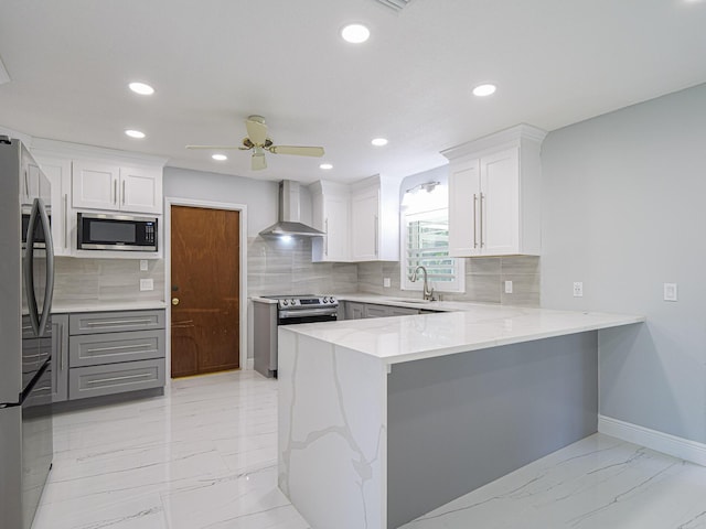 kitchen featuring wall chimney exhaust hood, white cabinetry, appliances with stainless steel finishes, and kitchen peninsula