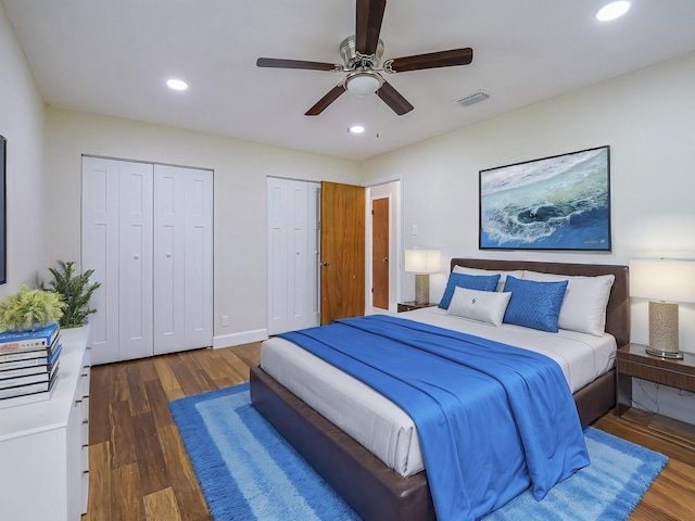 bedroom with multiple closets, dark wood-type flooring, and ceiling fan